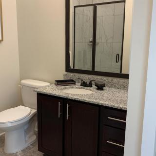 A modern bathroom with a granite countertop, dark wood cabinetry, and a shower with glass doors.