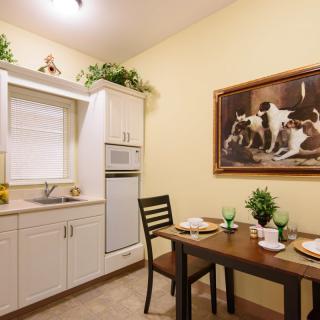 A cozy kitchen with a dining area featuring a small table set for two and decorated with greenery and framed artwork on the wall.