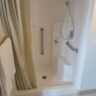 A bathroom with a shower and bathtub combination featuring grab bars and a handheld showerhead.