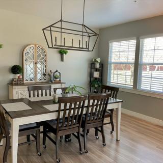 A cozy dining room with a wooden table and chairs, illuminated by a decorative chandelier, with natural light streaming in through the windows.