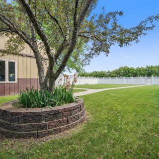 A well-maintained lawn with a tree surrounded by a circular brick planter, adjacent to a building and white fence.
