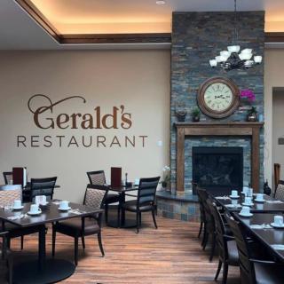 The interior of Gerald's Restaurant features a cozy dining area with neatly arranged tables and chairs, a decorative fireplace, and a wall clock.