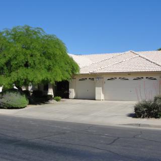 A suburban house with a large driveway and garage, surrounded by desert landscaping.