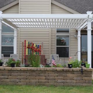 A cozy outdoor space featuring a white pergola, potted plants, and a decorative flag.