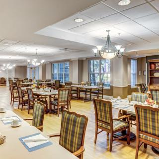 A spacious dining room with neatly arranged tables and chairs, featuring chandeliers and large windows.