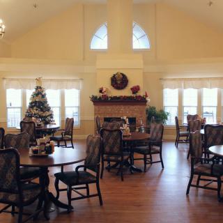 A cozy dining room with a festive Christmas tree and a warm fireplace surrounded by tables and chairs.