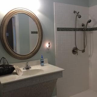 A bathroom with an oval mirror, a sink, and a shower area.