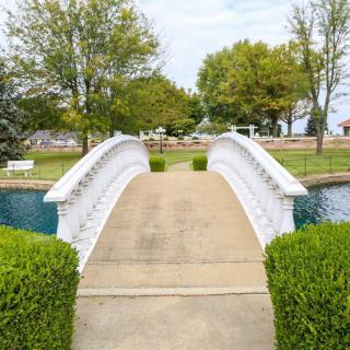 A white bridge in a scenic garden surrounded by lush greenery and a tranquil pond.