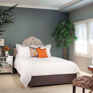 A cozy bedroom with a neatly made bed, accent pillows, and decorative plants.