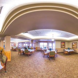 A spacious dining area with tables and chairs, featuring carpeted flooring and ceiling lights.