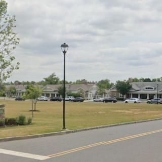 A suburban street view with a lamppost, grassy area, and several buildings under a cloudy sky.