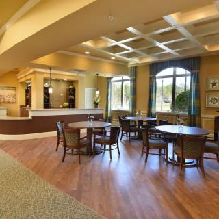 A spacious and well-lit lobby area with tables and chairs, featuring large windows and elegant decor.