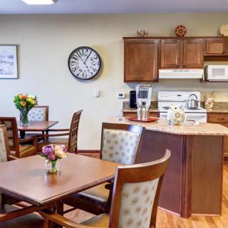 A cozy kitchen and dining area featuring wooden cabinets, a clock, and tables adorned with flowers.