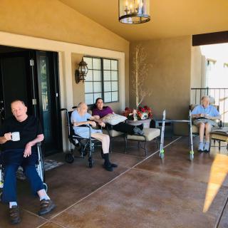 A group of elderly people sitting on a porch, enjoying a relaxing daytime conversation.