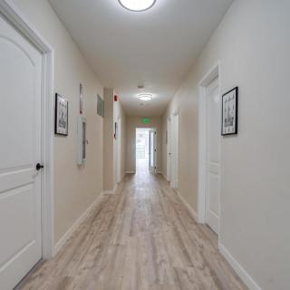 A long, well-lit hallway with multiple doors and framed artwork on the walls.