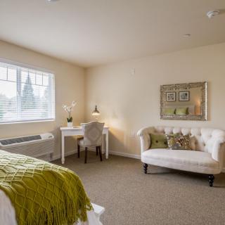 A cozy bedroom with a desk and sofa, decorated in soft neutral tones.