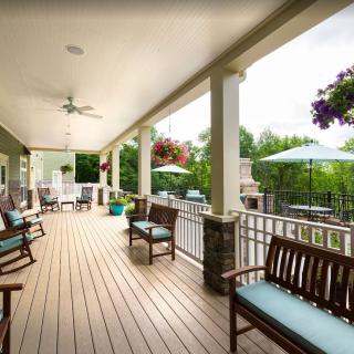 A spacious covered porch with wooden benches and hanging plants, perfect for relaxation.