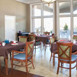 A well-lit dining room with several tables and chairs, featuring large windows.