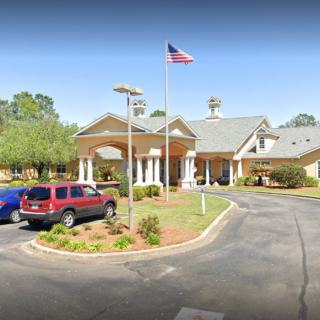A building with a circular driveway and parking area, featuring a flagpole with an American flag.