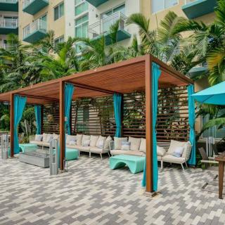 A tropical outdoor lounge area with cabanas and patio furniture, surrounded by palm trees.