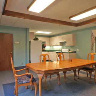 A well-lit dining area with a wooden table and chairs adjacent to a kitchen.