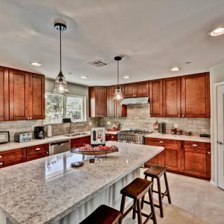 A modern kitchen featuring wood cabinets, a marble countertop island with seating, and stainless steel appliances.