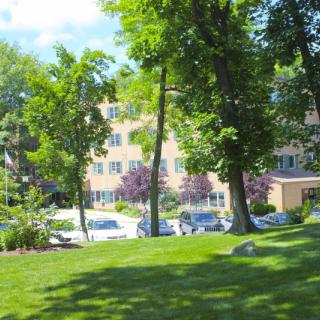 A sunny view of a building surrounded by trees and a parking lot.