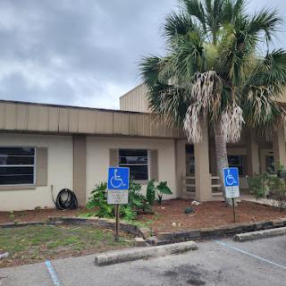 A view of a building with handicap accessible parking spaces and palm trees in the foreground under a cloudy sky.