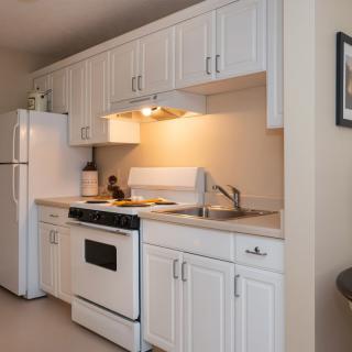 A compact kitchen with white cabinets, a stove, refrigerator, and sink.