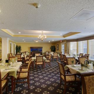 An elegant dining room with neatly arranged tables and chairs, featuring a chandelier and patterned carpet.