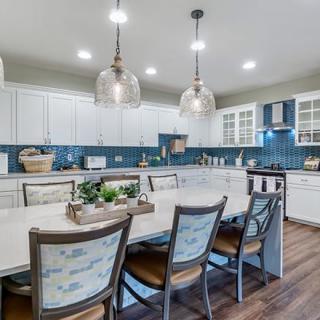 A modern kitchen with white cabinets, blue backsplash, and a spacious dining area.