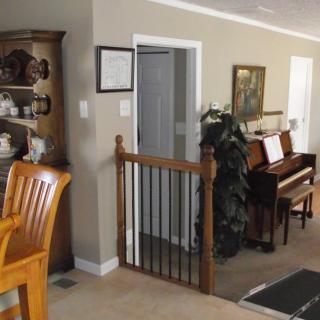 A cozy living room featuring a wooden chair, a piano, and a decorative shelf with a baby gate in the doorway.