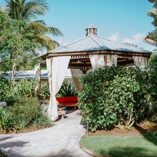 A serene tropical gazebo surrounded by lush greenery and palm trees.