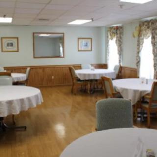 An empty dining room with round tables covered in white tablecloths and wooden chairs arranged around them.