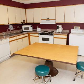 A cozy kitchen with a wooden table and teal stools, featuring essential appliances.