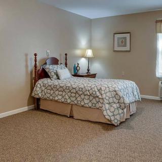 A well-lit bedroom with a single bed, nightstand, and a lamp by the window.