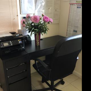 A tidy office setup with a desk, chair, printer, and a vase of flowers.