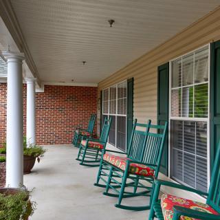 A cozy porch with green rocking chairs and cushioned seats.