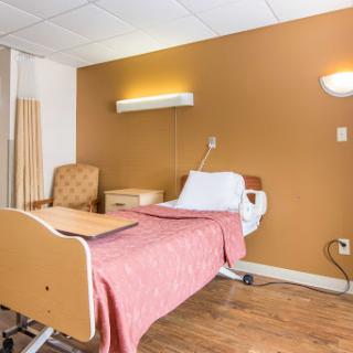 A clean and well-lit hospital patient room with a bed, armchair, and bedside lighting.