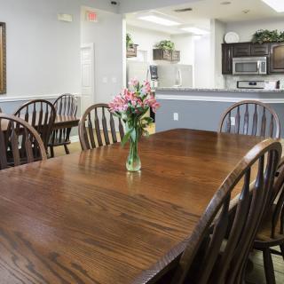 A cozy dining area featuring a wooden table and chairs, with a vase of flowers as the centerpiece, adjacent to a modern kitchen.