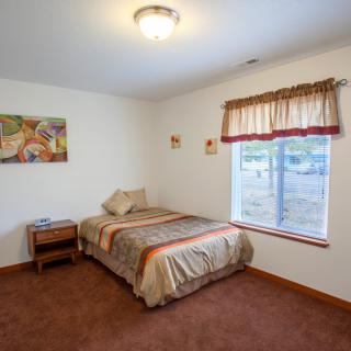 A cozy bedroom with a single bed, a nightstand, and a window with drapes, featuring wall art for decoration.