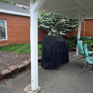 A covered grill sitting on a patio beside some outdoor seating and greenery.