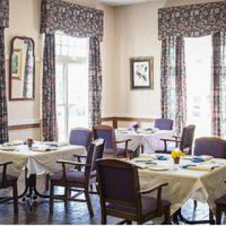 A cozy dining room with neatly arranged tables and chairs, featuring elegant curtains and artwork on the walls.