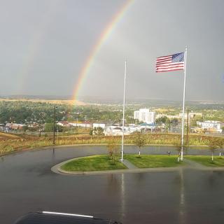 A double rainbow arches over a landscape with an American flag waving in the foreground.
