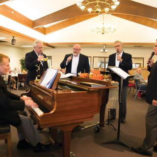 A group of musicians performing indoors, featuring a pianist and singers.