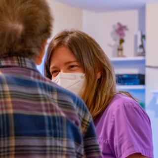 A healthcare professional wearing a mask engages in conversation with an elderly person.