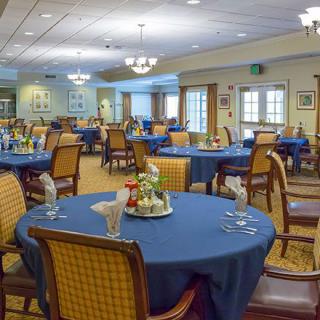 A well-set dining room with blue tablecloths and neatly arranged chairs, ready for guests.