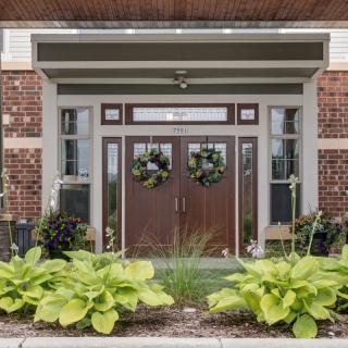 A welcoming entrance with double doors adorned with wreaths, surrounded by lush greenery and brickwork.