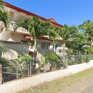 A residential building with palm trees and a fence on a sunny day.