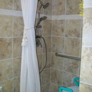A tiled shower area with a curtain and grab bar for safety.